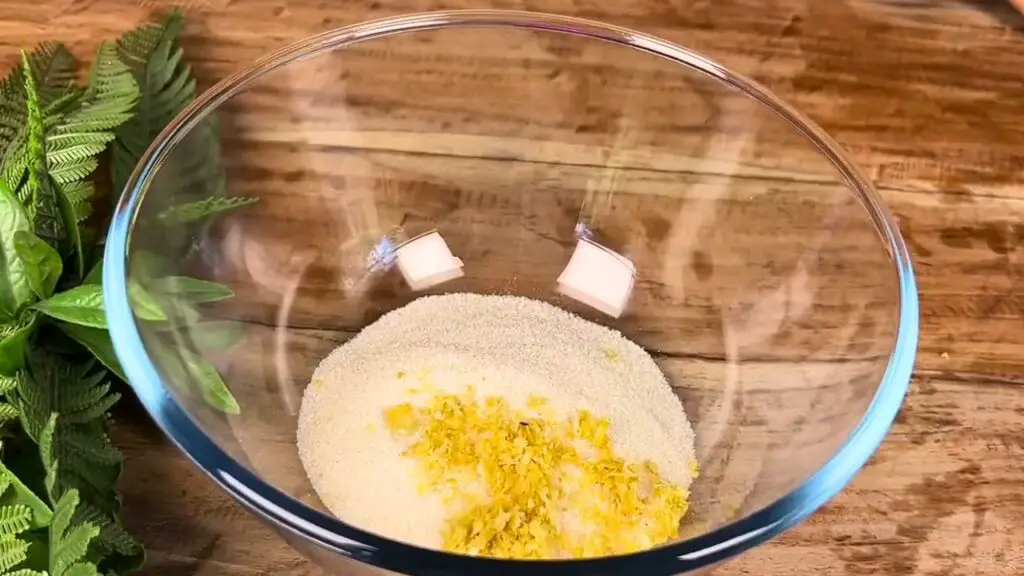 Starbucks lemon loaf recipe ingredients with fresh lemon zest and sugar combined in a glass mixing bowl.