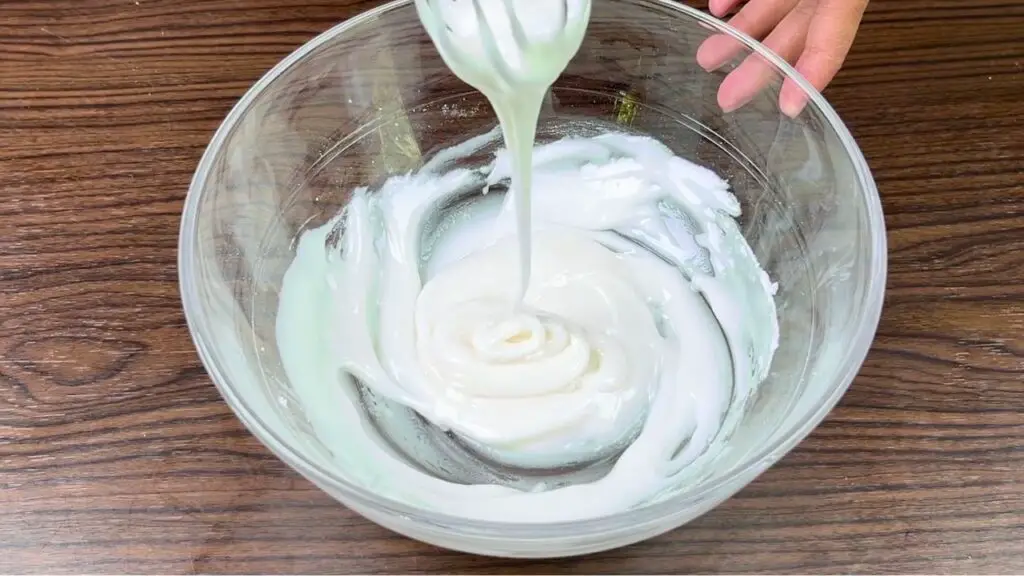 Thick lemon glaze being whisked in a glass bowl until smooth for topping a homemade lemon cake.