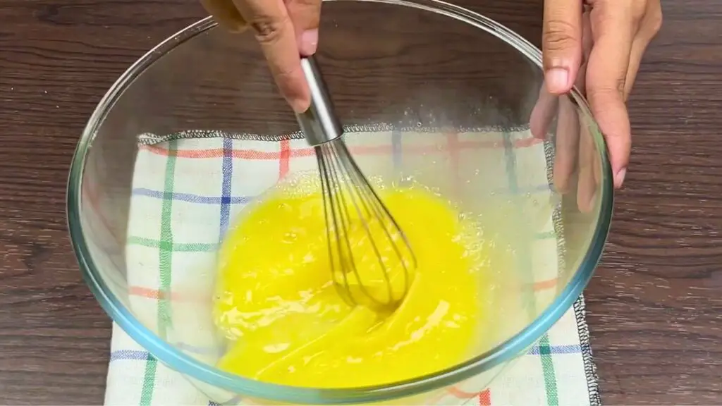 Whisking eggs with salt in a glass bowl for condensed milk loaf cake batter.
