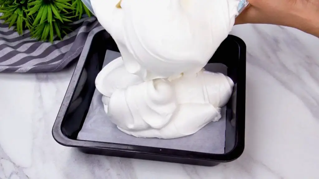 Yogurt ice cream recipe mixture being poured into a parchment-lined freezer-safe pan before freezing.