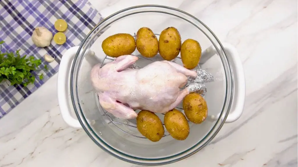 Air fryer roast chicken placed breast-side down with potatoes in a glass bowl.