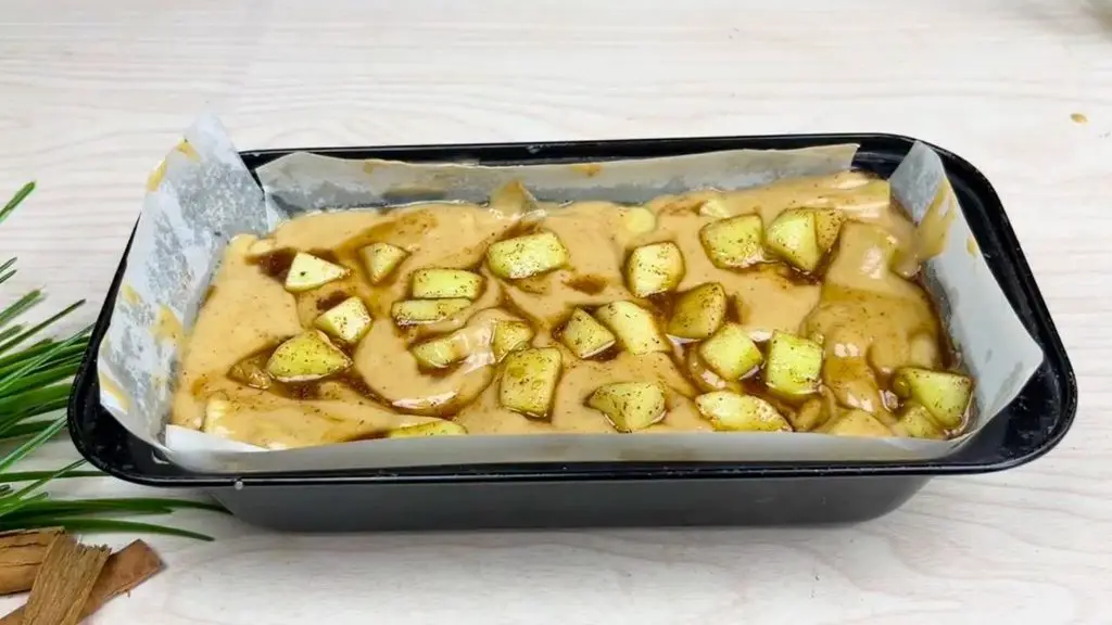 Apple cinnamon cake batter topped with cinnamon-coated apple pieces and gently swirled to distribute the apples through the loaf.