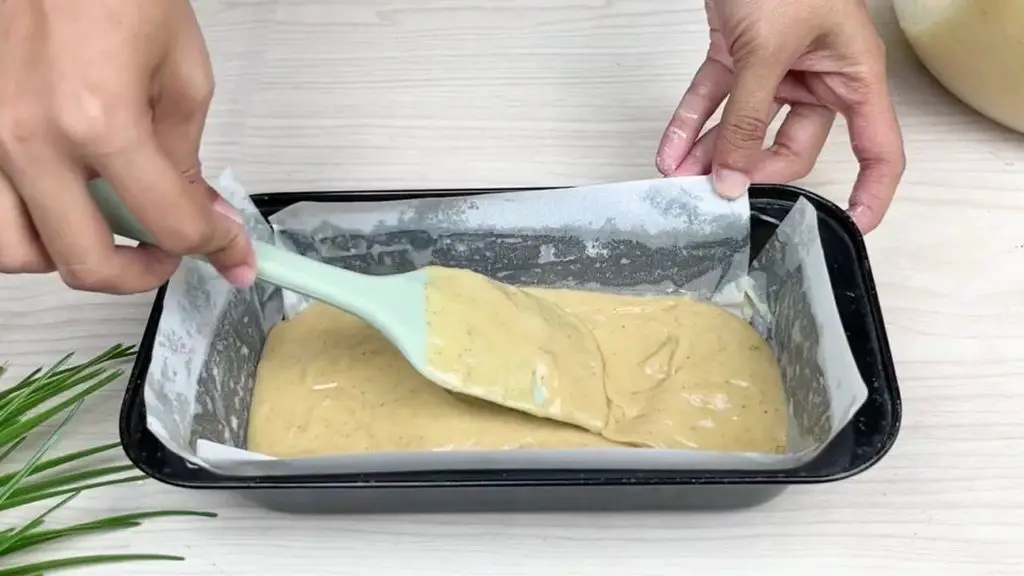 Apple cinnamon loaf cake batter spread evenly in a parchment-lined loaf pan before adding the cinnamon apple filling.