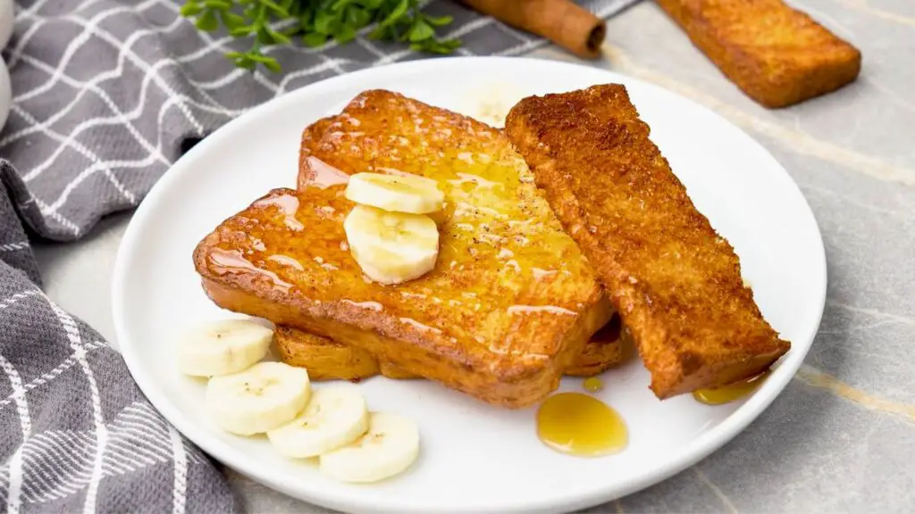 Crispy air fryer French toast topped with banana slices and a drizzle of syrup.