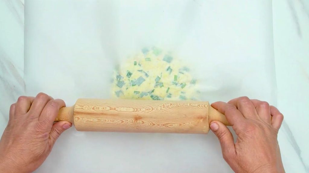 How to make crackers by rolling green onion dough thinly between sheets of parchment paper.