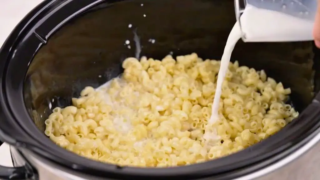 Slow Cooker Macaroni and Cheese Recipe with milk and evaporated milk being poured over cooked macaroni in the slow cooker.
