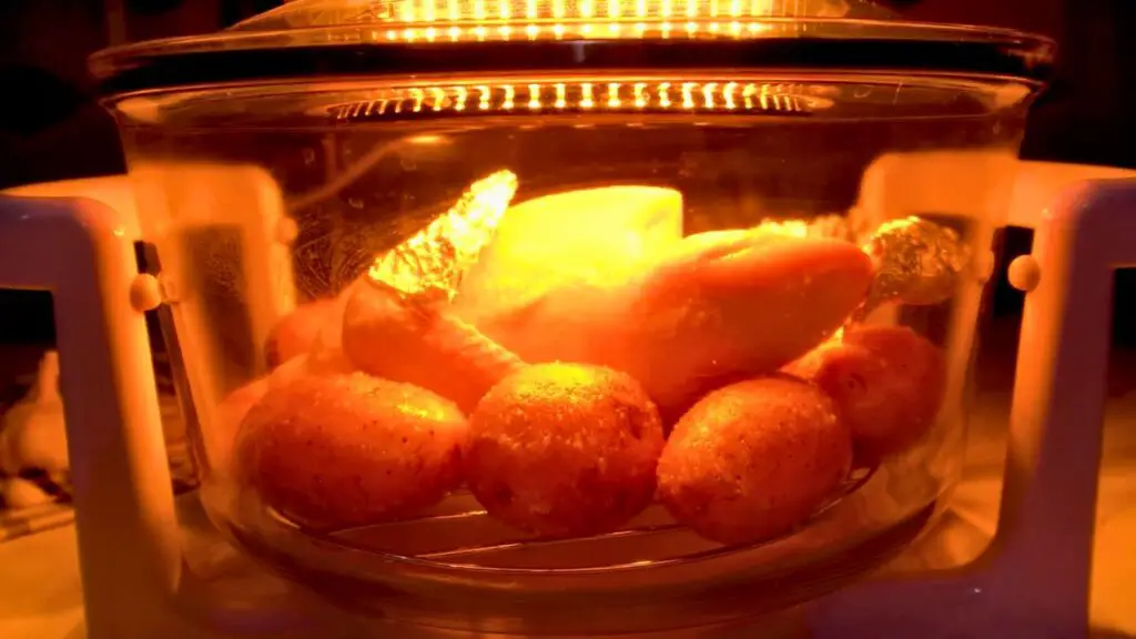 Whole chicken and potatoes cooking in a glass bowl air fryer.
