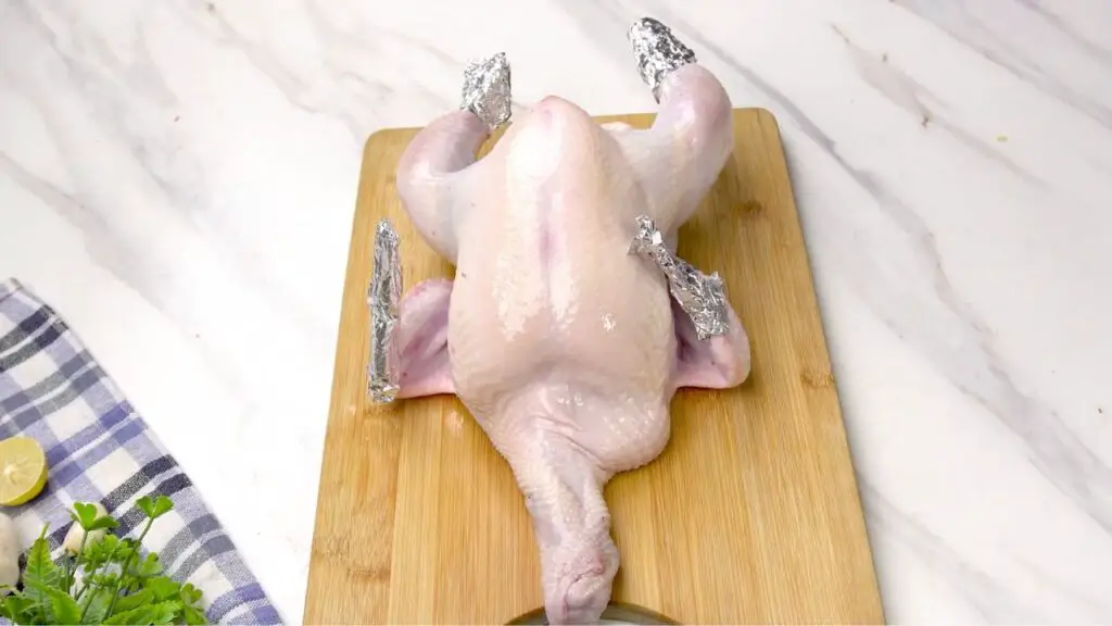 Wrapping the wing tips and drumstick ends with foil for air fryer whole chicken.