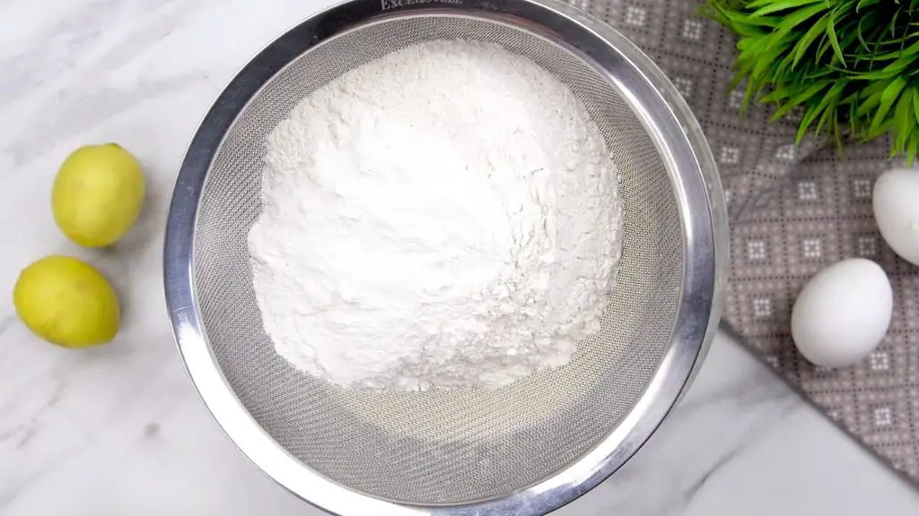 Yogurt cake recipe with all-purpose flour and baking powder being sifted to create a smooth, light cake batter.