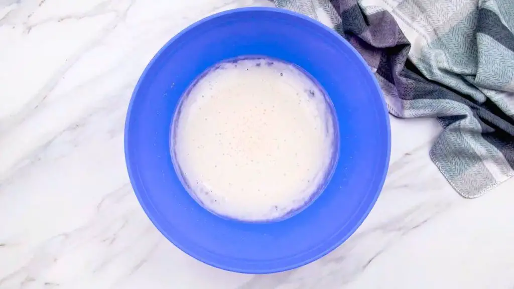 Activated yeast mixture with bubbles and foam in a blue bowl for an air fryer bread recipe.