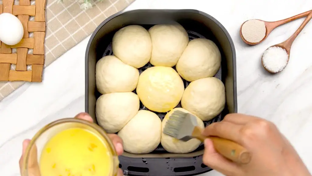 Brushing risen brioche buns with beaten egg before cooking in the air fryer.