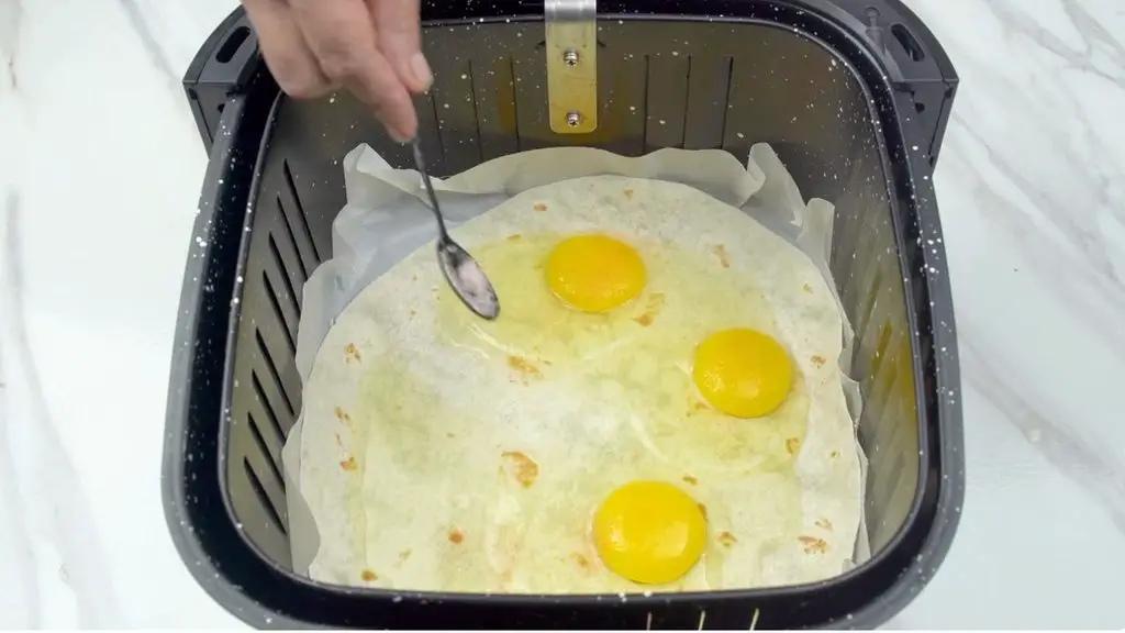 Crack the eggs directly onto the tortilla for this air fryer breakfast pizza, then break the yolks and gently spread the eggs across the tortilla before adding the toppings.