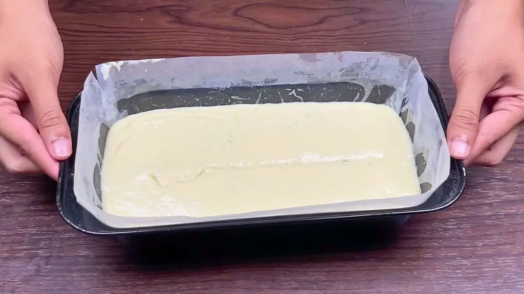 Lemon cake batter spread evenly in a parchment-lined loaf pan ready for baking.