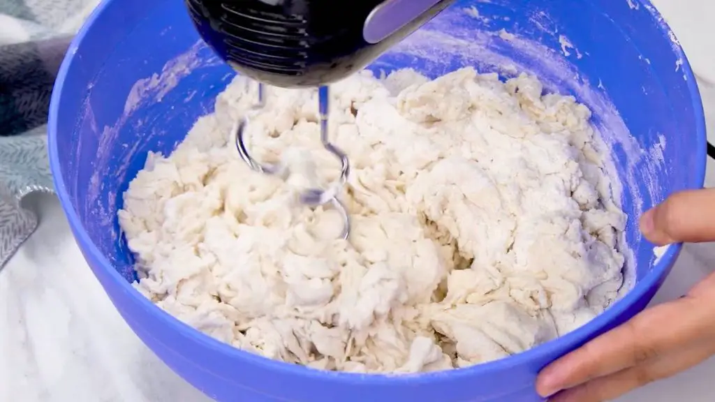 Mixing bread dough with an electric hand mixer and dough hooks in a blue bowl for an air fryer bread recipe.