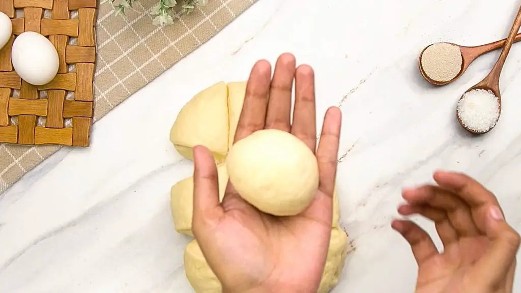 Shaping dough into a smooth round ball for an easy brioche bun recipe.