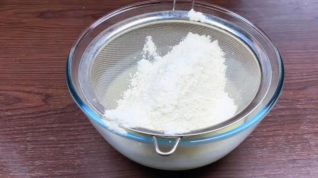 Sifting flour into cake batter while making a moist lemon cake.