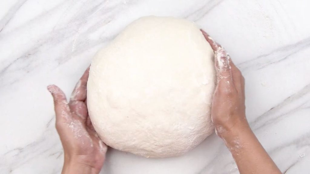 Soft risen bread dough being lifted onto a lightly floured surface before shaping for homemade air fryer bread.