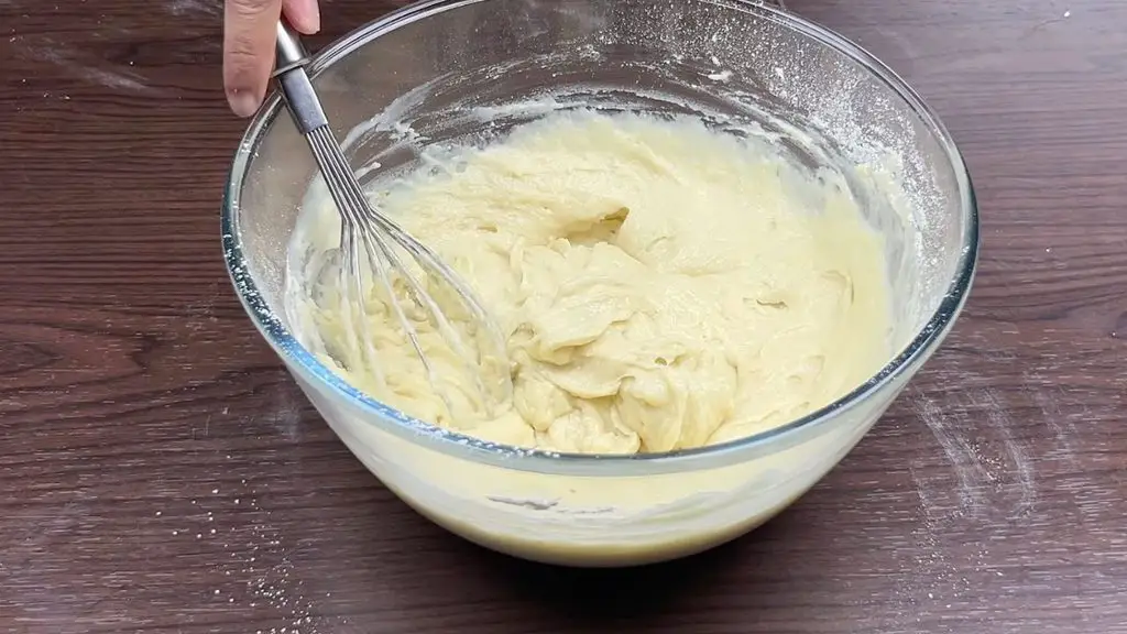 Thick lemon cake batter being mixed in a bowl while checking the consistency.