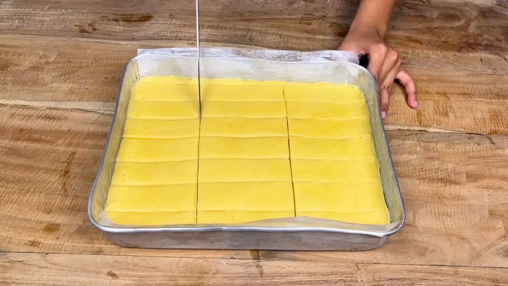 Cutting shortbread cookie dough into evenly sized fingers in a parchment-lined baking tray.