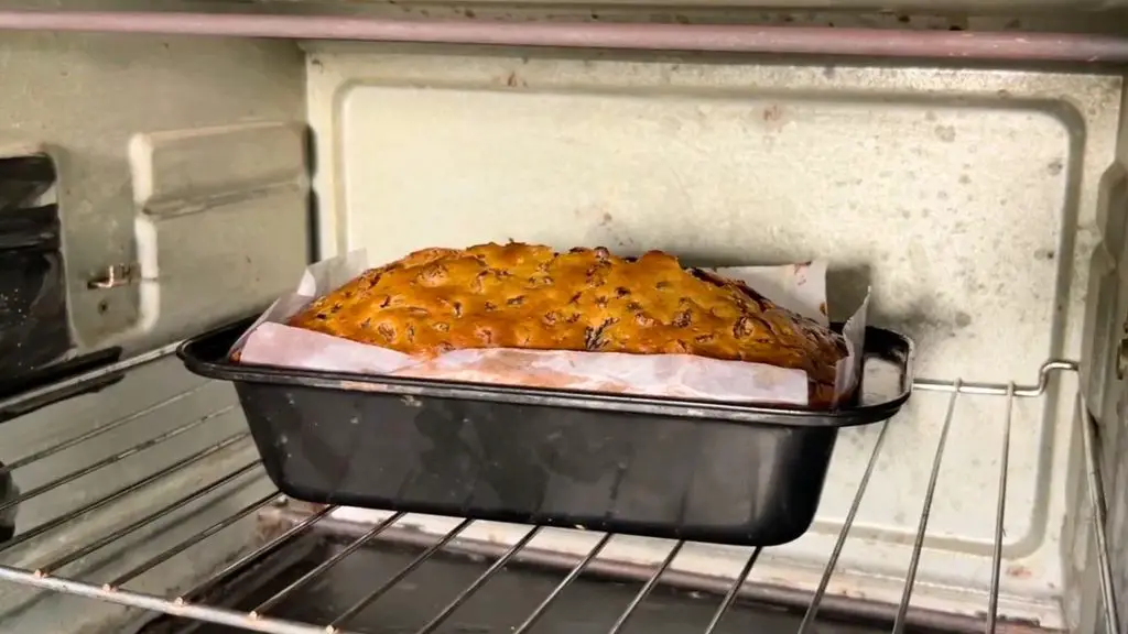 Grandma's traditional fruit cake baking in a parchment-lined loaf pan inside the oven, with a golden brown top and visible dried fruit.