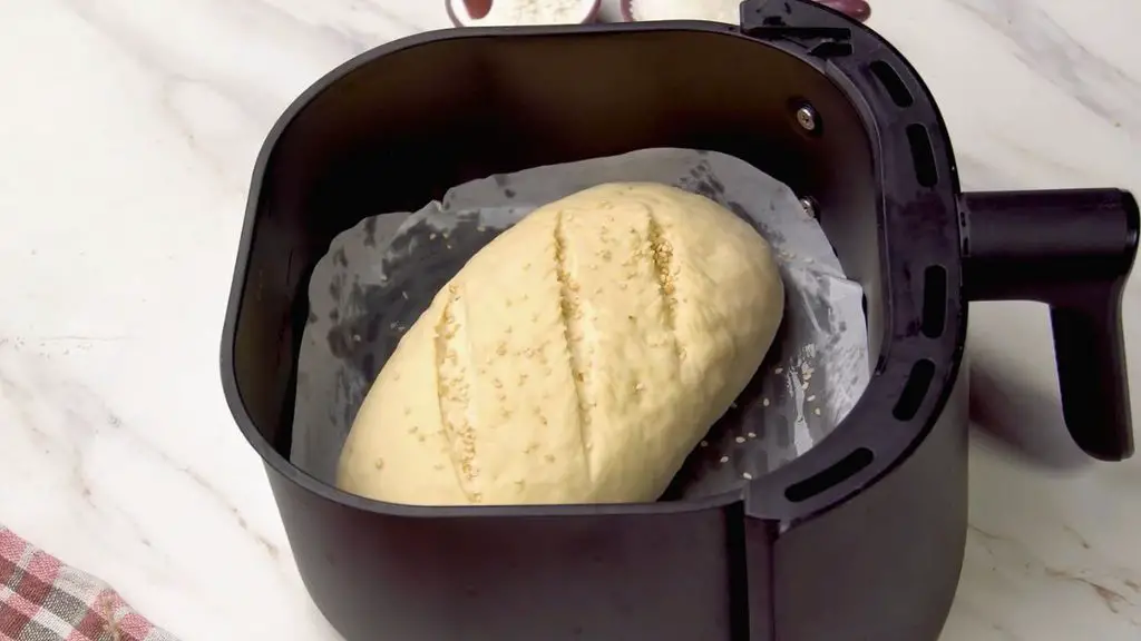 How to make bread in air fryer with shaped dough topped with white sesame seeds and placed in a parchment-lined air fryer basket.