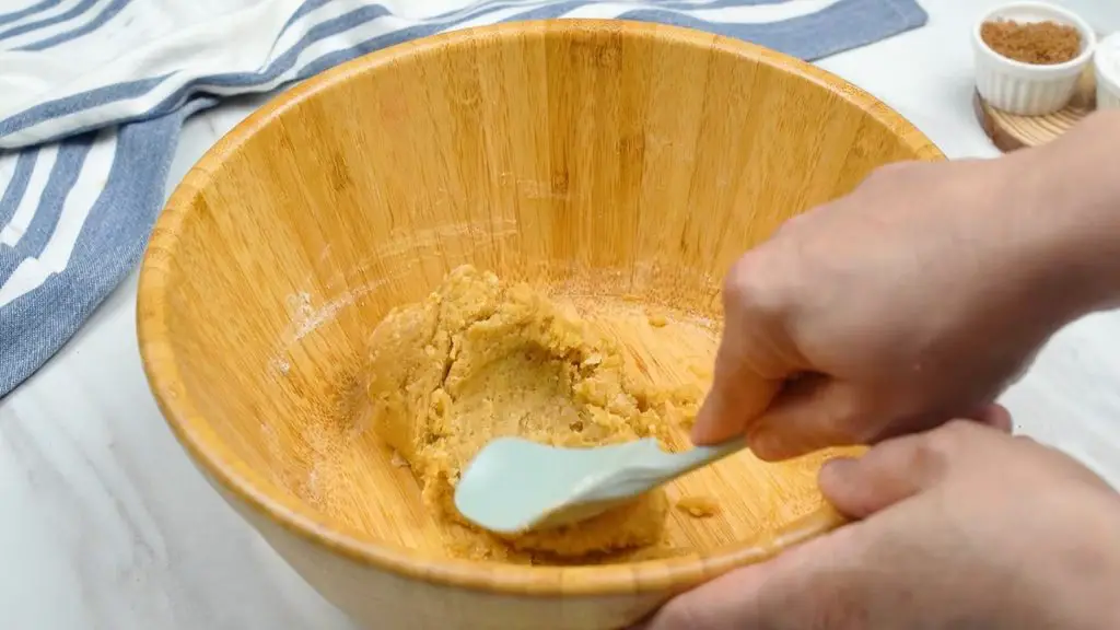 Mixing flour, baking soda, and salt into soft chocolate chip cookie dough with a spatula in a wooden bowl for air fryer chocolate chip cookies.