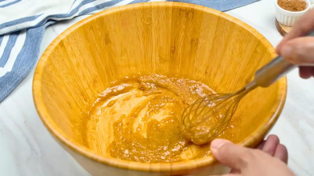 Mixing melted butter, brown sugar, and granulated sugar with a whisk in a wooden bowl for a single serve chocolate chip cookie recipe.