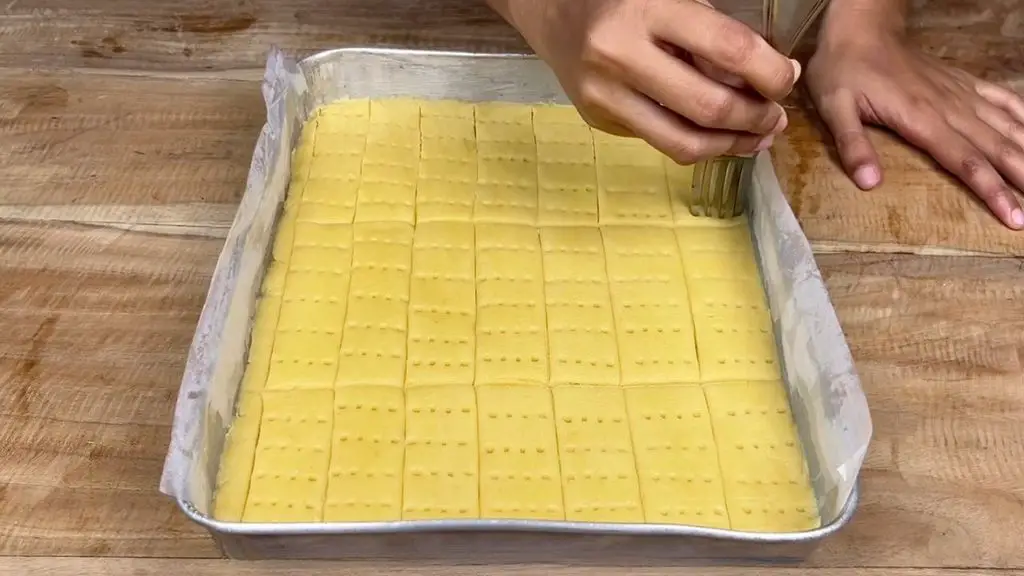 Pricking buttery shortbread cookie dough with a fork in a parchment-lined baking tray.