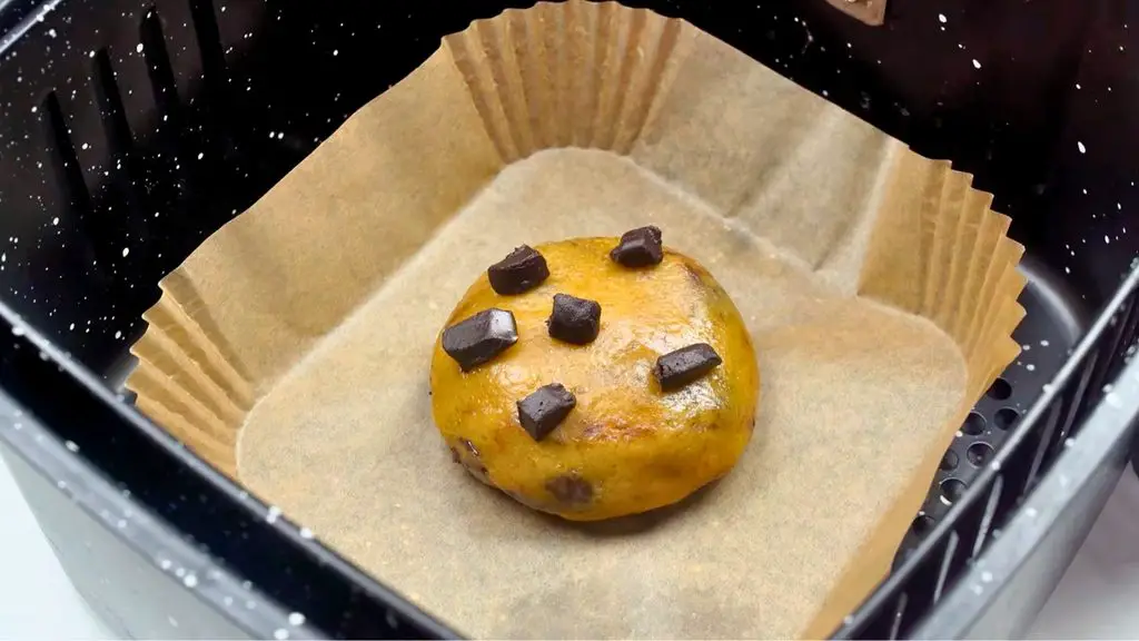 Single serve air fryer chocolate chip cookie dough topped with chocolate chunks, placed in the center of a parchment-lined air fryer basket before baking.