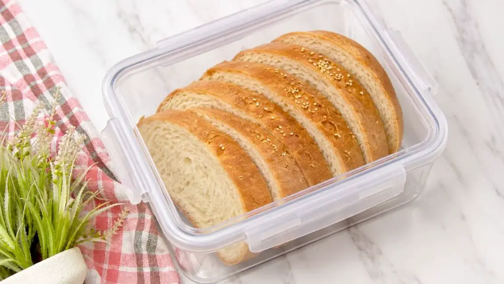 Sliced air fryer milk bread with a golden brown sesame seed crust and soft, fluffy interior stored in a clear airtight container.