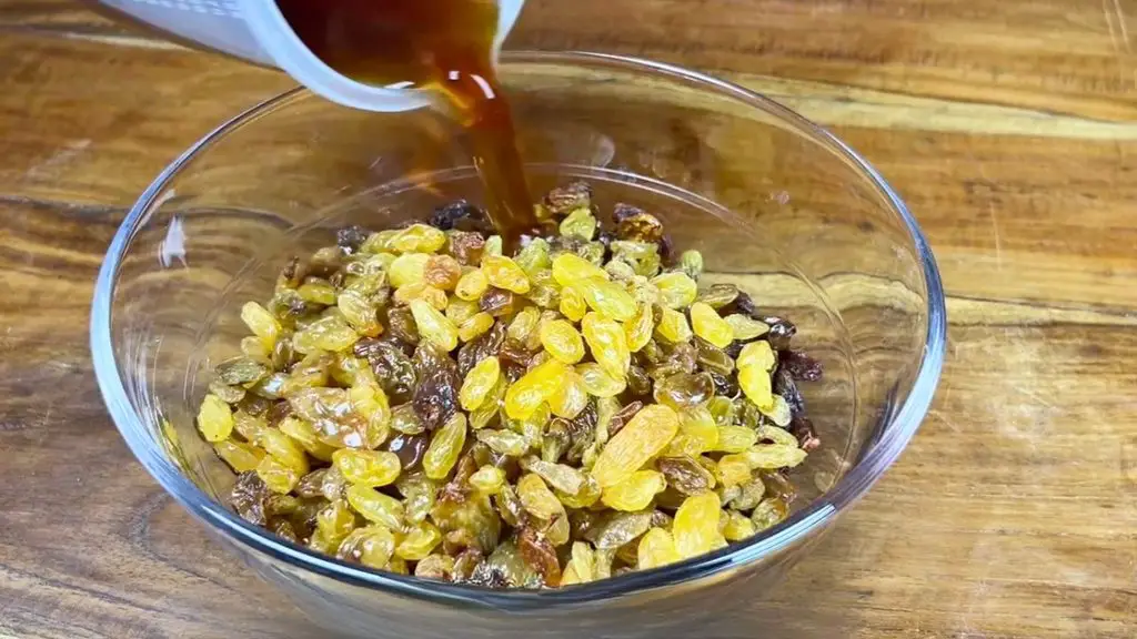 Strong hot black tea being poured over sultanas and raisins in a glass bowl to soak overnight for an old fashioned fruit cake recip