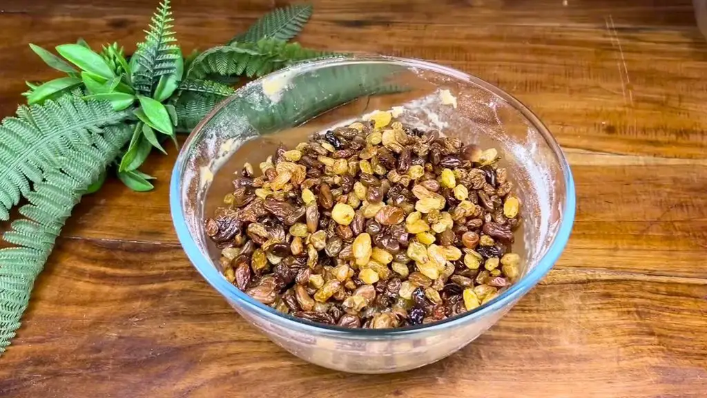Tea-soaked sultanas and raisins added to a glass bowl of cake batter, ready to be folded together for a traditional fruit cake recipe.